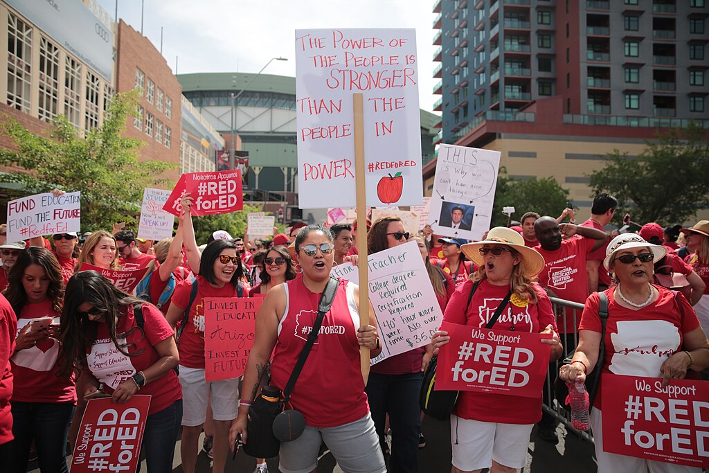 Arizona teachers wearing red t-shirts emblazoned with #redfored stirke and rally holding signs.